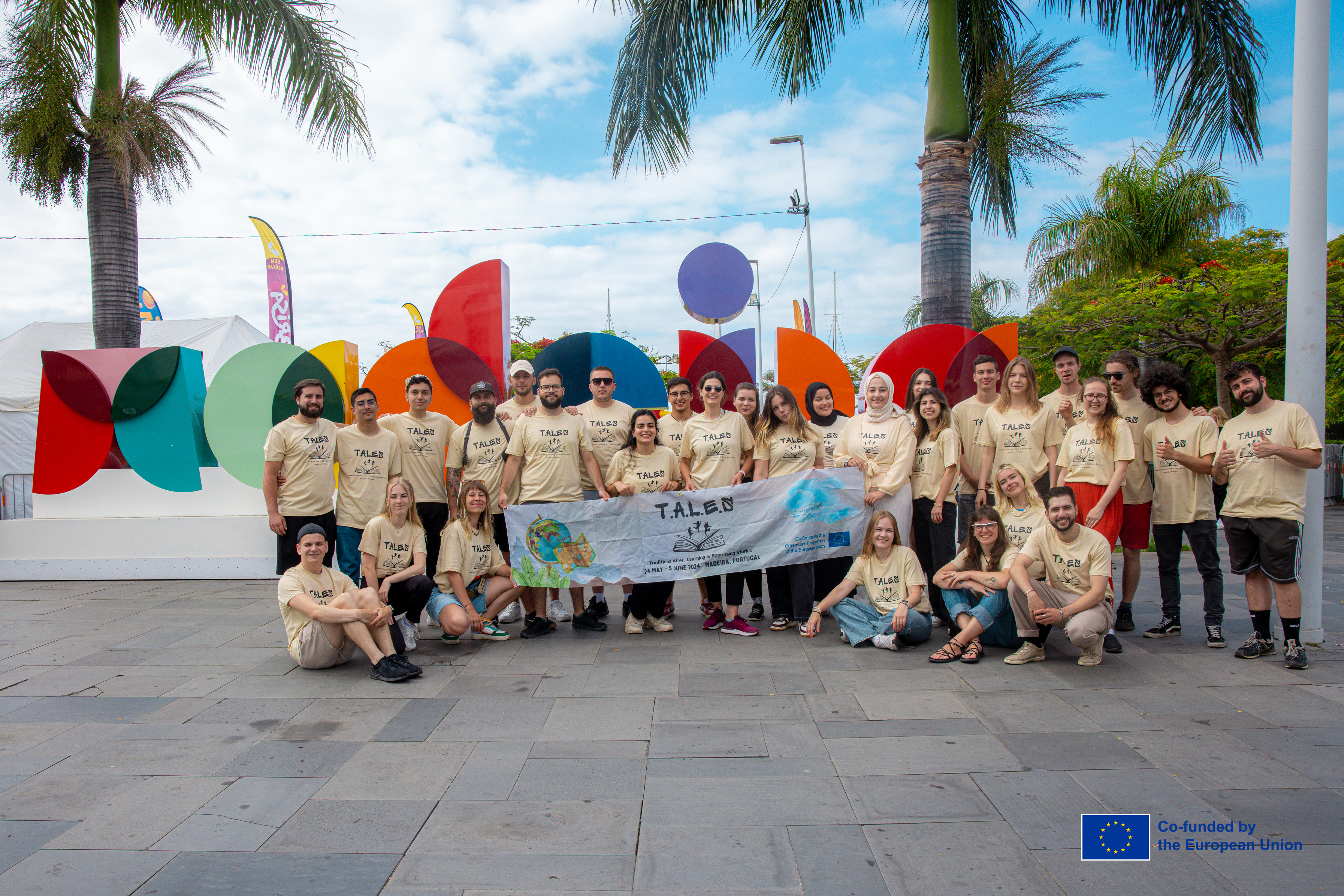 TALES 1.0 participants posing with their project banner beneath palm trees